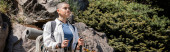 Young short haired female hiker in casual clothes with backpack holding trekking poles and looking away while standing with nature at background, woman trekking across vast landscapes, banner Poster #662549684