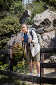 Young short haired woman traveler in casual clothes with backpack holding trekking poles and looking away while standing with nature at background, woman trekking across vast landscapes Poster #662549694