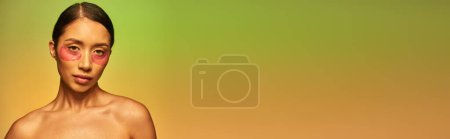 Foto de Campaña de cuidado de la piel, mujer asiática joven con cabello moreno y hombros desnudos posando y mirando a la cámara en el fondo verde, cuidado de la cara, parches para los ojos hidratantes, piel brillante, pancarta - Imagen libre de derechos