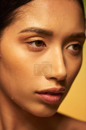 Wassertropfen im Gesicht, Nahaufnahme einer jungen asiatischen Frau mit nasser Haut, die auf grünem Hintergrund wegschaut, Hautfeuchtigkeit, Schönheitskampagne, Perfektion, Wellness, konzeptionelle 