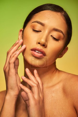 Wassertropfen im Gesicht, Nahaufnahme einer jungen asiatischen Frau mit feuchter Haut, die das Gesicht auf grünem Hintergrund berührt, geschlossene Augen, Hautfeuchtigkeit, Schönheitskampagne, Perfektion, Wohlbefinden, konzeptionelle 