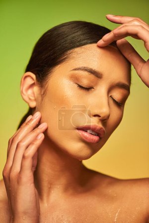 Wassertropfen im Gesicht, Nahaufnahme einer jungen Asiatin mit geschlossenen Augen und feuchter Haut auf grünem Hintergrund, Hautfeuchtigkeit, Schönheitskampagne, Perfektion, Wellness, konzeptionelle 