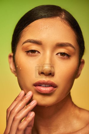 Wassertropfen im Gesicht, Nahaufnahme einer jungen asiatischen Frau mit feuchter Haut vor der Kamera auf grünem Hintergrund, Hautfeuchtigkeit, Gesichtspflegekampagne, Perfektion, Wohlbefinden, konzeptionelle 