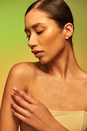 hydration, young asian woman with bare shoulders touching wet body and posing on gradient background, closed eyes, skincare campaign, beauty model, brunette hair, glowing skin 
