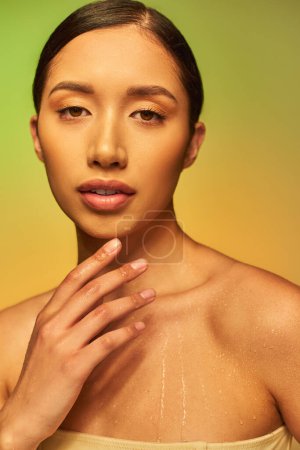 Hydratation, asiatische Frau mit nackten Schultern und nassem Körper posiert auf Gradienten Hintergrund, Beauty-Kampagne, Blick in die Kamera, junges Modell, brünettes Haar, glühende Haut 