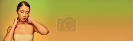 Foto de Fotografía de belleza, mujer asiática con cabello moreno y hombros desnudos posando sobre fondo degradado, verde y naranja, cuidado de la piel, piel brillante, belleza natural, modelo joven, radiante, pancarta - Imagen libre de derechos