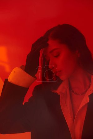 Foto de Moda moderna, estilo y fotografía, joven modelo asiático en camisa blanca y chaqueta posando en guantes detrás de cristal rojo, ojos cerrados, estilo personal, tendencia juvenil, conceptual - Imagen libre de derechos