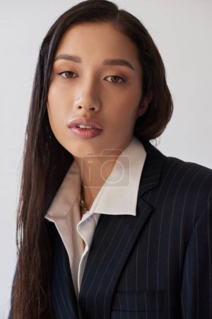 asiatische Schönheit, junge Frau in weißem Hemd und Blazer schaut vereinzelt in die Kamera auf graue, jugendliche, perfekte Haut, stilvoller Look, Mode nach vorne, Porträt, brünettes Model im Studio
