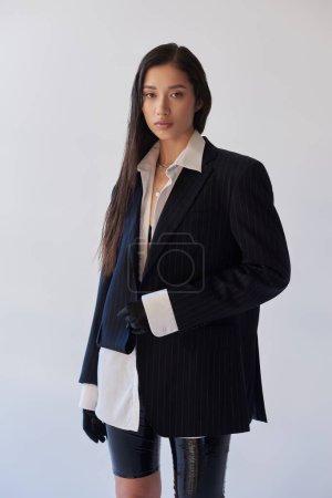 Téléchargez les photos : Jeune mode, femme asiatique brune en tenue tendance posant sur fond gris, chemise blanche, blazer et gants noirs, jeune mannequin, photographie studio, conceptuel - en image libre de droit