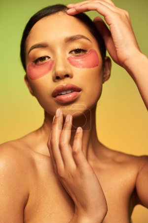 jolie et brune asiatique posant avec des patchs sur fond vert, dégradé, beauté, peau désintoxiquée, soin du visage, épaules nues, routine de soins de la peau, peau éclatante, portrait 