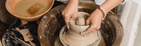 Vue grand angle de jeune femme potier moulage argile humide tout en travaillant avec roue de poterie et bol avec de l'eau et éponge dans un atelier de céramique, atelier de poterie espace de travail et concept d'artisanat, bannière