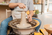 Cropped view of female artisan in apron pouring water on clay while working on pottery wheel in blurred ceramic workshop at background, artisan creating unique pottery pieces Stickers #663415430
