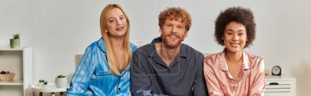 Photo for Open relationship, polygamy, understanding, three adults, happy redhead man and multicultural women in pajamas sitting on bed at home, cultural diversity, acceptance, bisexual, banner - Royalty Free Image