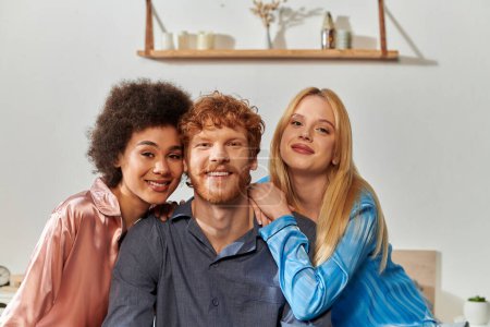 polyamory concept, open relationship, polygamy, portrait of three adults, happy redhead man and multicultural women in pajamas looking at camera, cultural diversity, acceptance, bisexual 
