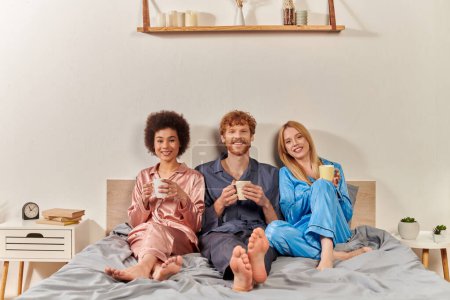 non traditional family concept, polygamy, redhead man and interracial women in pajamas holding cups of coffee, morning routine, bisexual, understanding, three adults, cultural diversity, acceptance 