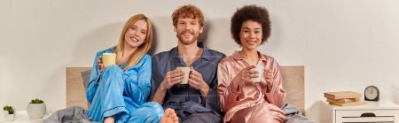 concepto de relación abierta, poligamia, hombre pelirrojo y mujeres multiculturales felices en pijamas sosteniendo tazas de café, rutina de la mañana, bisexual, comprensión, tres adultos, diversidad cultural, bandera