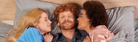 polyamory concept, man and interracial women in pajamas waking up together, morning, under blanket, bedroom, cultural diversity, bisexual, open relationship, polygamy, top view, banner
