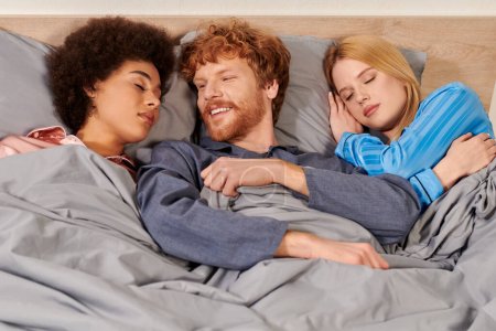 Photo for Non traditional relationship, polygamy, three adults, happy redhead man waking up near multicultural women, threesome, cultural diversity, acceptance, bisexual - Royalty Free Image