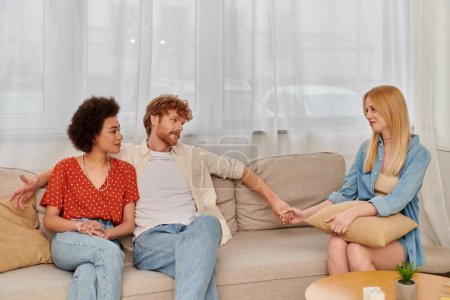 polygamy concept, acceptance, alternative relationships, african american woman sitting with redhead man holding hand with blonde lover, cultural diversity, love triangle, freedom in relationship 