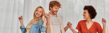 Photo for Polygamy, happy multicultural women and bearded man holding hands, having fun, dancing in living room, love and diversity in relationships, modern family, acceptance and bonding, banner - Royalty Free Image