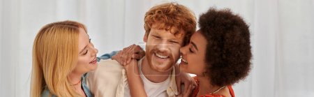 non traditional family, polygamy, three adults, happy interracial women hugging redhead man, threesome, cultural diversity, acceptance, bonding and love, multiracial lovers, banner