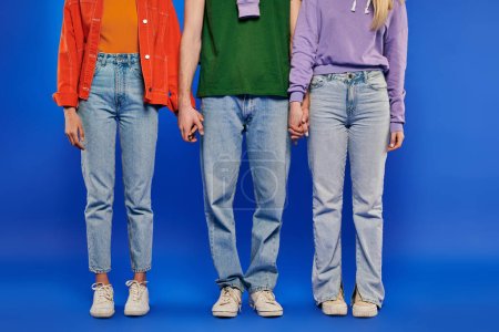 alternative family, polygamy, partial view of polyamory three people, young man and women holding hands on blue background, studio shot, vibrant clothes, romantic, modern relationships 