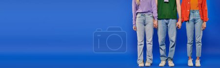alternative relationships, polygamy, partial view of polyamory three people, young man and women holding hands on blue background, studio shot, vibrant clothes, modern love triangle, banner