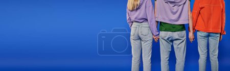 polygamy, back view of polyamory three people, young man and women holding hands on blue background, studio shot, denim fashion, love triangle, cropped shot, bonding, banner 