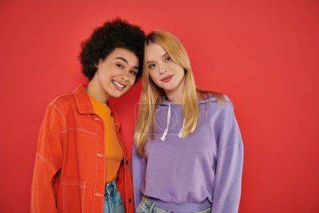 cultural diversity, happy multicultural women looking at camera on coral background, blonde and brunette, diverse friends, sisterhood, friendship goals, studio shot, multiracial people 