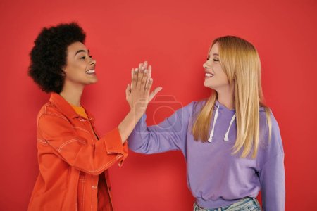 Photo for Cultural diversity, cheerful multicultural women giving high five on coral background, blonde and brunette, diverse friends, sisterhood, friendship goals, studio shot, female friends - Royalty Free Image