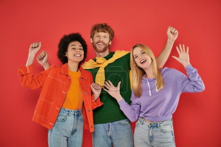 polyamorous concept, polygamy lovers, young man and multicultural women celebrating on coral background, studio shot, denim fashion, love triangle, bonding and acceptance 