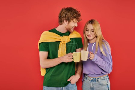 happy young couple holding cups of coffee on coral background, morning routine, vibrant colors, stylish outfits, modern family, people holding mugs with hot drink, husband and wife 
