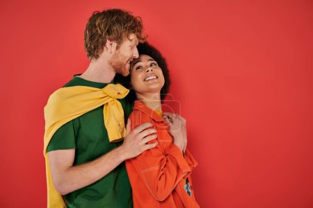 Photo for Interracial couple hugging and smiling on coral background, cultural diversity, vibrant colors, stylish outfits, youth and fashion, interracial people looking at each other, african american woman - Royalty Free Image