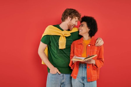 interracial couple hugging and reading book on coral background, cultural diversity, vibrant colors, stylish outfit, youth and intelligence, multicultural people spending lovely time together