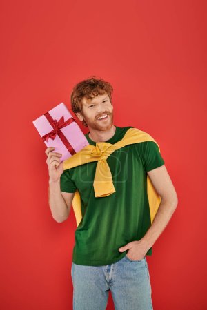 vacances, homme rousse heureux avec barbe posant en tenue décontractée sur fond corail, tenant boîte cadeau, occasions festives, cadeau enveloppé, mode et tendance, style urbain, bonheur 