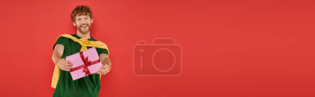 Feier, glücklicher rothaariger Mann mit Bart posiert in lässiger Kleidung auf Korallengrund, hält Geschenkbox, festliche Anlässe, verpacktes Geschenk, Mode und Trend, urbaner Stil, Urlaub, Banner 