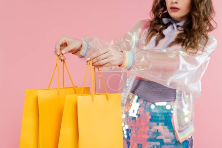 Photo for Cropped view of young woman carrying shopping bags on pink background, concept photography, consumerism, stylish outfit, model in skirt with sequins and transparent jacket, retail therapy - Royalty Free Image