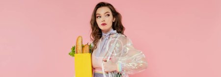 housewife concept, beautiful young woman holding reusable mesh bag with groceries, stylish wife doing daily house duties, standing on pink background, looking away, role play, banner 