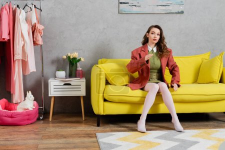 concept photography, posing like a doll, well dressed young woman with wavy hair sitting on yellow couch, gesturing, stylish house interior, vase with tulips, looking at camera, housewife lifestyle 