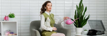 Photo for Eco-friendly, housekeeping concept, woman acting like a doll, beautiful woman watering plant, green thumb, sitting on armchair and holding toy rabbit, housewife with pink watering can, banner - Royalty Free Image