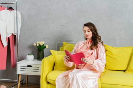 Konzeptfotografie, Frau mit brünetten welligen Haaren, häusliches Leben, attraktive Hausfrau liest Buch, sitzt auf gelbem Sofa, komfortables Wohnen, häuslicher Lebensstil 