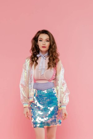 Photo for Beautiful woman with wavy hair posing like a doll on pink background, conceptual photography, girly outfit, model in skirt with sequins and transparent jacket looking at camera - Royalty Free Image