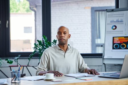 chronic illness, bold african american businessman with eye syndrome looking at camera near laptop on desk, myasthenia gravis, dark skinned office worker, diversity and inclusion, entrepreneurship 