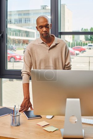 myasthenia gravis syndrome, bold african american businessman with ptosis syndrome looking at computer monitor, dark skinned office worker in casual attire standing at desk, inclusion 