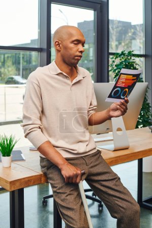 Téléchargez les photos : Inclusion, syndrome de myasthénie grave, homme d'affaires afro-américain audacieux debout avec canne à pied et regardant les cartes près de l'écran d'ordinateur, employé de bureau à la peau foncée en tenue décontractée - en image libre de droit