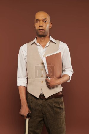 inclusion, bold african american man with myasthenia gravis syndrome, standing with walking cane and holding folder, dark skinned man with chronic disease on brown background 