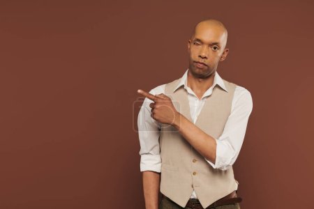 inclusion, african american man with myasthenia gravis syndrome looking at camera, bold dark skinned man with chronic disease pointing away on brown background with copy space, showing something 