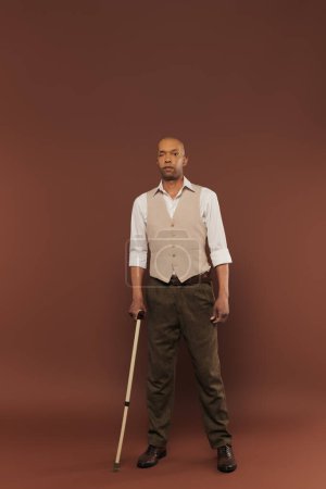 Photo for Real people, bold african american man with myasthenia gravis syndrome standing with walking cane on brown background, standing and looking at camera, diversity and inclusion, physical impairment - Royalty Free Image