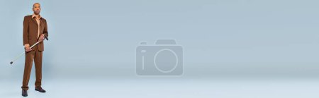 Ptosis-Syndrom, langer, kräftiger afrikanisch-amerikanischer Mann mit Myasthenia gravis auf grauem Hintergrund, dunkelhäutige Person im Anzug mit Gehstock, Vielfalt und Inklusion, Banner 