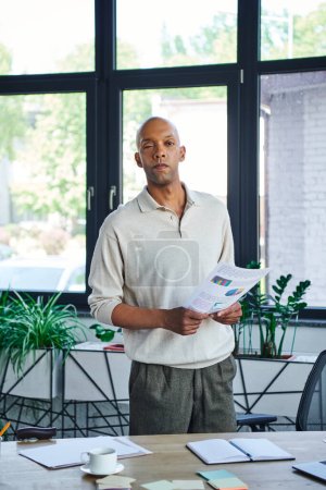 myasthenia, dark skinned office worker with ptosis syndrome holding charts, inclusion, bold african american businessman with eye syndrome looking at camera, standing near green plants in office 